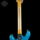 Close-up of the back of a blue electric guitar showing the tailpiece, pickups, and part of the natural wood neck against a black background.