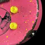 Close-up of a pink guitar body with yellow control knobs, yellow paint splatters, and a distressed black edge showing wood underneath.