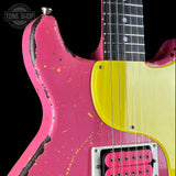 A close-up of a pink electric guitar body with a bright yellow pickguard, distressed finish, and part of the dark fretboard. A Tone Shop watermark is visible in the top-left corner.