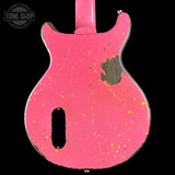 A close-up of a pink electric guitar body with a distressed finish, featuring yellow and orange paint splatter details and a dark wood patch on the upper right side, shown against a black background.