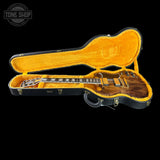 A double-cutaway electric guitar with a glossy dark wood finish, displayed inside an open black hard case with a bright yellow-orange plush lining. The Tone Shop logo is visible in the top-left corner.