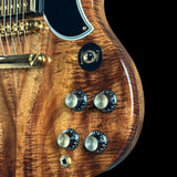 Close-up of a guitar body showing a rich flamed wood grain finish, gold hardware, and control knobs against a black background.