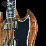 Close-up of an electric guitar body showing a rich flamed maple wood finish, black pickguard, gold hardware, and part of the fretboard on a black background.