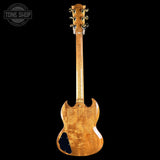 The back view of a Gibson SG electric guitar with a natural figured wood finish, displayed against a solid black background. A Tone Shop watermark is visible in the top-left corner.