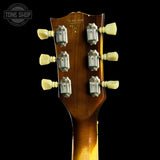 Close-up of a guitar headstock with tuning pegs on a black background, featuring the Tone Shop logo.