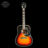 A Gibson acoustic guitar with a sunburst finish, featuring a black floral pickguard and white binding, shown against a solid black background with a Tone Shop watermark in the top left corner.