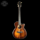 Acoustic guitar with a dark brown finish on a black background, featuring the Tone Shop logo.