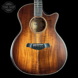Acoustic guitar with a dark brown finish on a black background, featuring the Tone Shop logo.