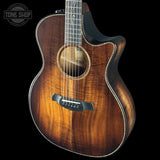 Acoustic guitar with a dark brown finish on a black background, featuring the Tone Shop logo.