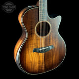Acoustic guitar with a dark brown finish on a black background, featuring the Tone Shop logo.