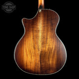Back view of a wooden acoustic guitar with a dark brown finish on a black background, featuring the Tone Shop logo.