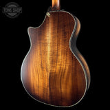 Back view of a wooden acoustic guitar with a dark brown finish on a black background.