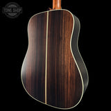 Back view of a wooden acoustic guitar with a visible brand logo in the corner.
