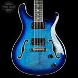 Blue electric guitar with a black pickguard on a black background, featuring 'Tone Shop' branding.
