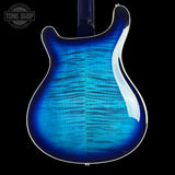 Blue electric guitar body with a clear finish on a black background, featuring the Tone Shop logo.