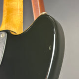 Close-up detail of an electric guitar body showing a glossy black finish, part of the wooden neck, and a silver hardware screw against a neutral gray background.