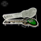 A green electric guitar inside an open black hard case with a gray velvet interior, photographed against a black background. A Tone Shop watermark is visible in the top-left corner.
