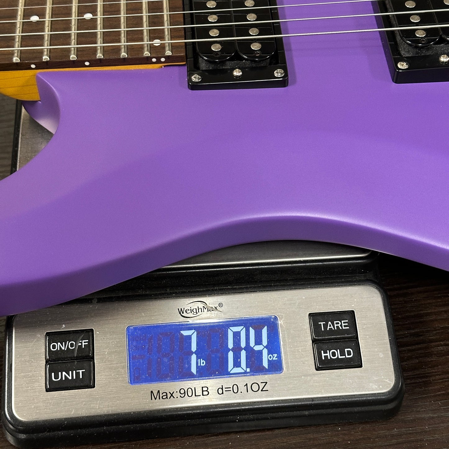Purple electric guitar on a digital scale displaying weight.