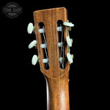Close-up of the headstock of a classical guitar, showing the six tuning pegs and strings against a solid black background.