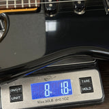 A digital scale displaying 8 lbs and 18 oz under a glossy black guitar body, with part of the guitar neck and pickups visible.