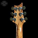 Close-up of the headstock of an electric guitar against a black background, showing six tuning pegs, a wood grain finish, and a Tone Shop watermark in the top left corner.