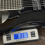 Digital scale displaying weight of a black electric guitar on a wooden surface