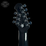 Close-up rear view of a black electric guitar headstock with six tuning pegs and visible 'Tone Shop' branding, shown against a solid black background.