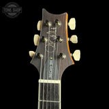Close-up of the headstock of a McCarty S-204 electric guitar against a black background, featuring a dark wood finish, six cream tuning pegs, and a white signature on the headstock.