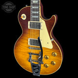 A Gibson Les Paul Custom electric guitar with a vibrant orange-to-brown sunburst finish, cream pickguard, and gold hardware, shown against a solid black background with a Tone Shop watermark in the top-left corner.
