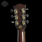 Close-up of the headstock of a Gibson acoustic guitar, showing six tuning pegs with gold and silver details and the Gibson logo on a black background.
