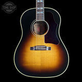 A classic acoustic guitar with a natural sunburst finish, featuring a dark brown pickguard and a white binding, shown against a solid black background with a Tone Shop watermark in the top left corner.
