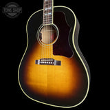 A classic acoustic guitar with a sunburst finish, featuring a bright amber center, dark brown outer edges, and a black pickguard. The neck is visible, showing fretboard inlays and strings, set against a solid black background with a Tone Shop watermark in the top left corner.