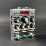 Silver audio effects pedal with knobs and display on a dark background