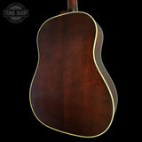 The back of an acoustic guitar with a rich dark brown wood finish and a thin cream-colored binding, shown against a solid black background. A Tone Shop watermark is visible in the top-left corner.