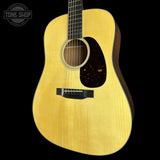 A natural wood acoustic guitar shown from the side against a solid black background, featuring a light yellow-gold spruce top, dark brown pickguard, and black bridge. A Tone Shop watermark is visible in the upper left corner.
