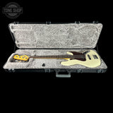 An open hard guitar case with a gray plush interior, holding a cream-colored bass guitar with a dark brown pickguard and yellow headstock. The case is photographed against a solid black background, with a Tone Shop watermark in the upper left corner.