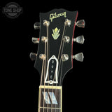 Close-up of a Gibson Dove acoustic guitar headstock in black, featuring gold script branding, a gold palm leaf logo, and silver tuning pegs against a black background.