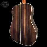 Acoustic guitar with a wooden finish on a black background, featuring the Tone Shop logo.