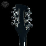Close-up of a guitar headstock with tuning pegs on a black background, featuring the Tone Shop logo.