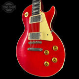 Red electric guitar with gold hardware on a black background, featuring 'Tone Shop' logo.