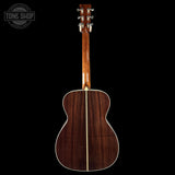 Acoustic guitar with a dark wood finish on a black background, featuring the Tone Shop logo.