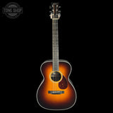 Acoustic guitar with a sunburst finish on a black background, featuring the Tone Shop logo.