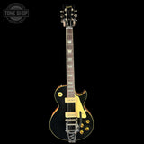 Electric guitar with a black finish and gold hardware on a white background