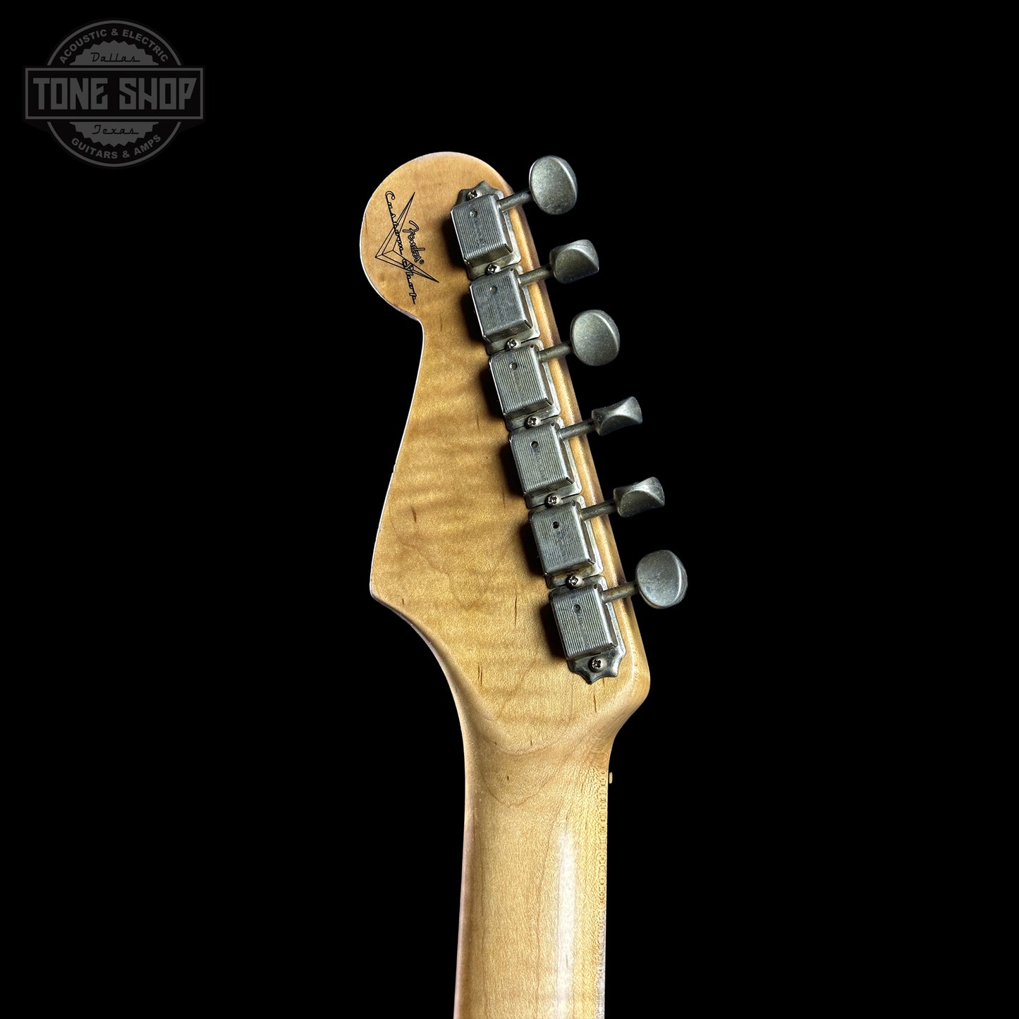 Close-up of a guitar headstock with tuning pegs on a black background, featuring the Tone Shop logo.
