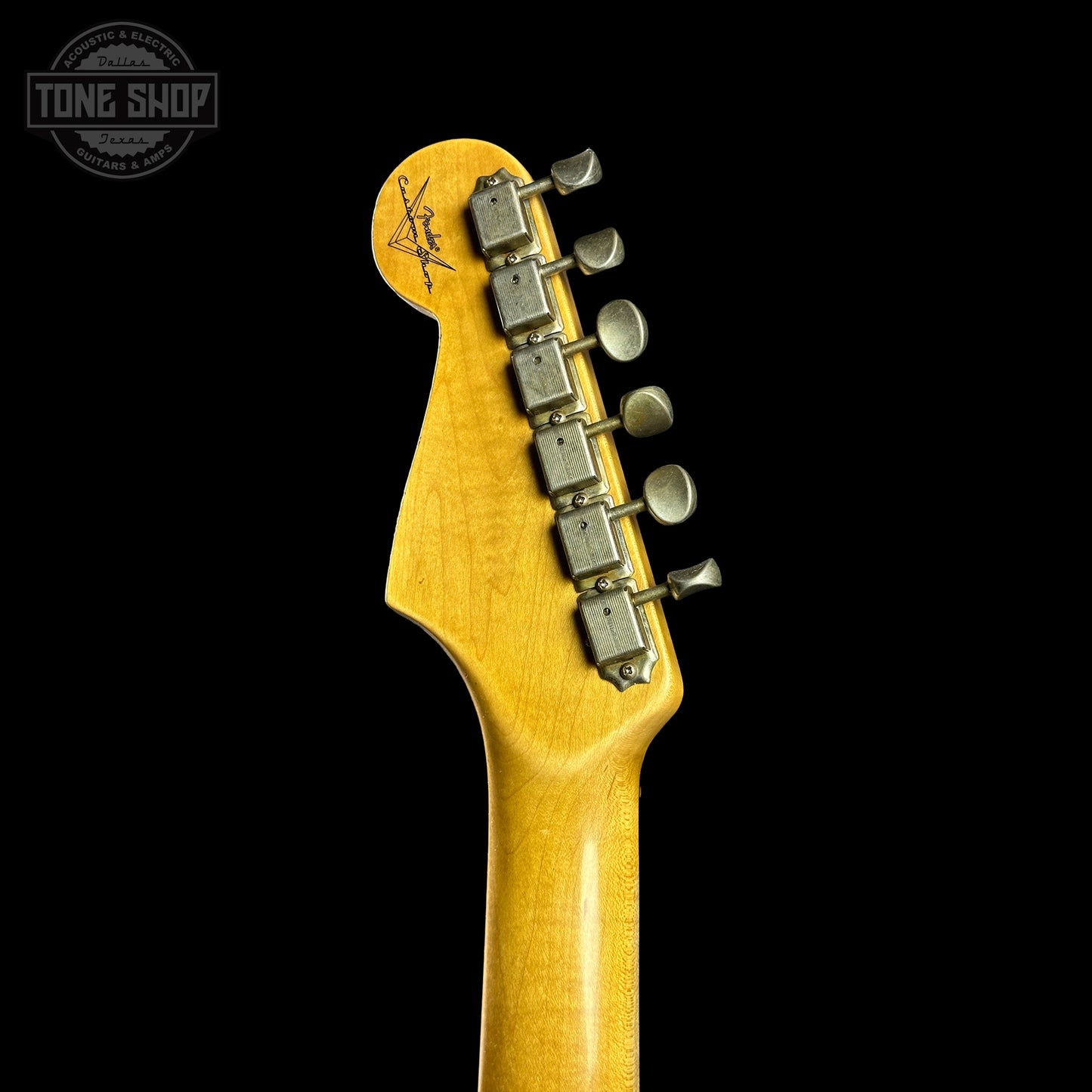 Close-up of a guitar headstock with tuning pegs on a black background, featuring the Tone Shop logo.