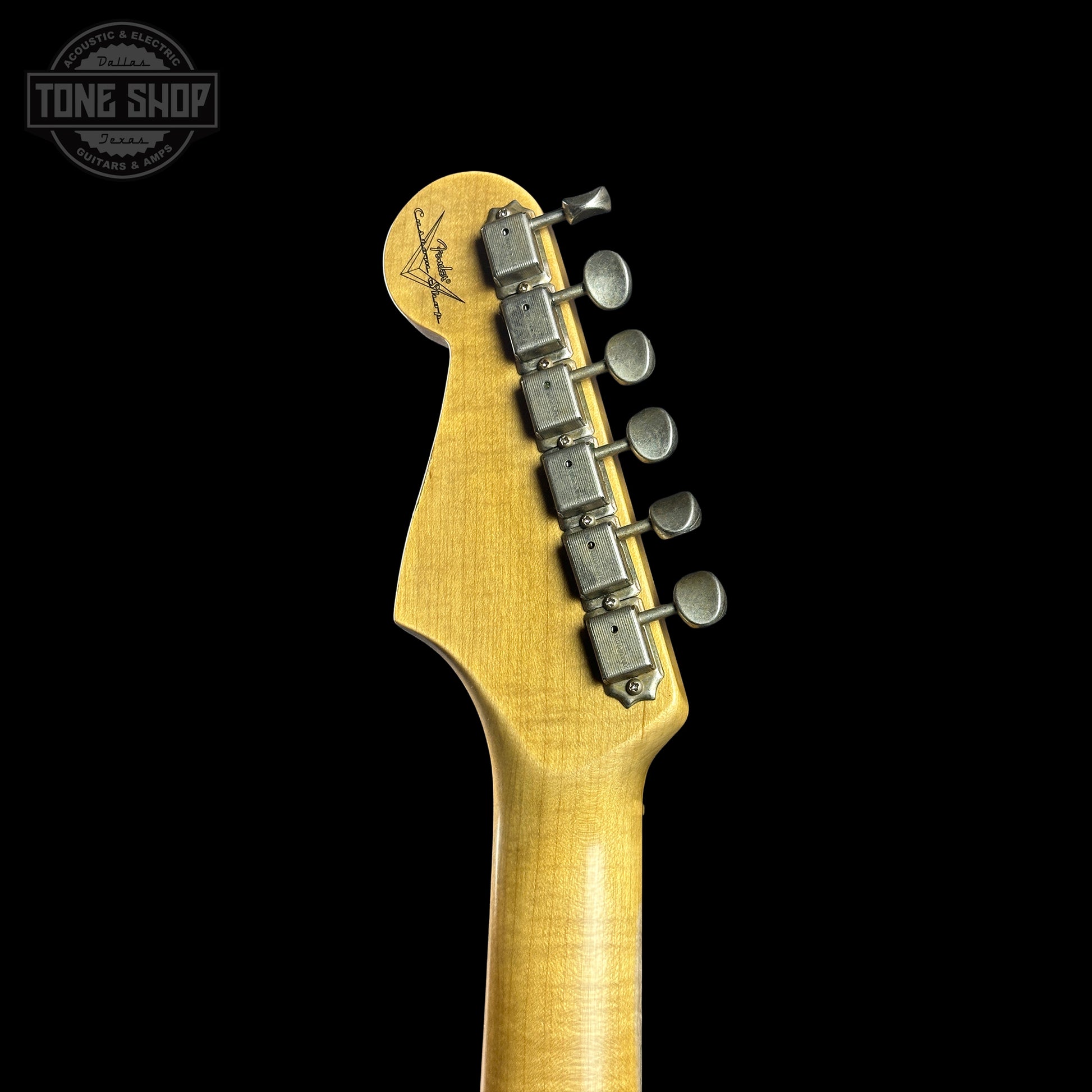 Close-up of a guitar headstock with tuning pegs on a black background, featuring the Tone Shop logo.