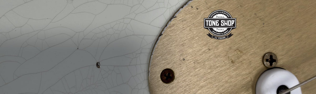 Close up details of white guitar with checked finish, and bronze pickguard with Tone Shop Guitars 11 Years badge at the top right corner.
