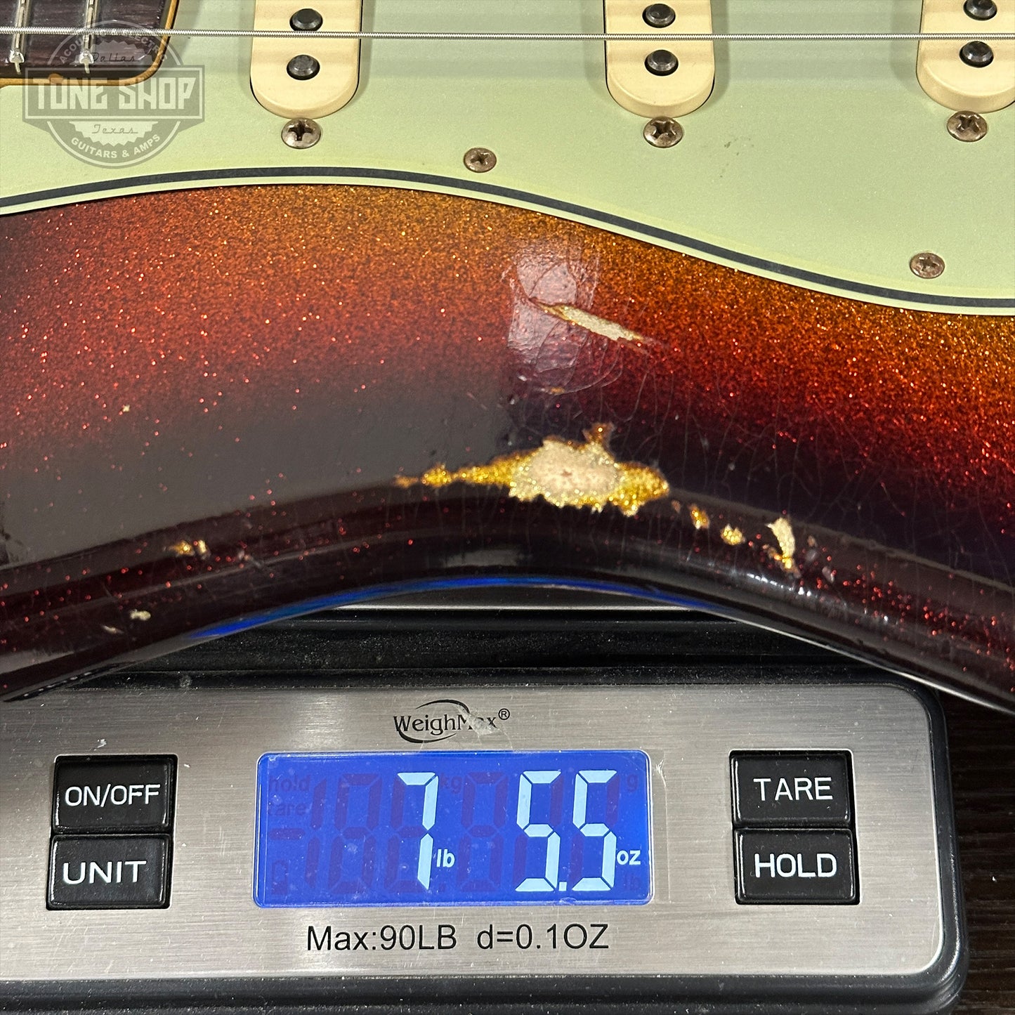 Guitar being weighed on a digital scale with a visible brand logo.