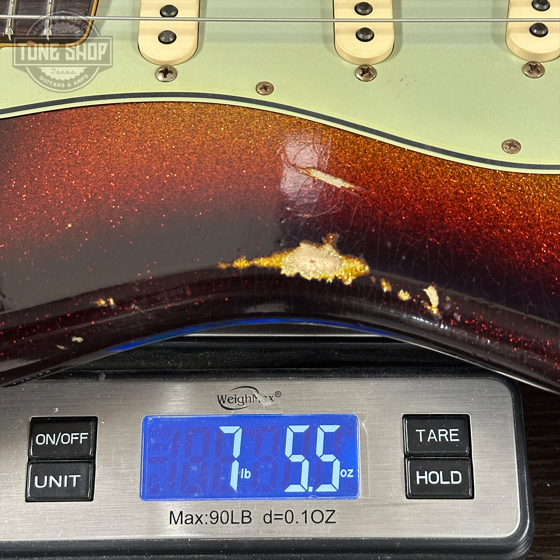 Guitar being weighed on a digital scale with a visible brand logo.