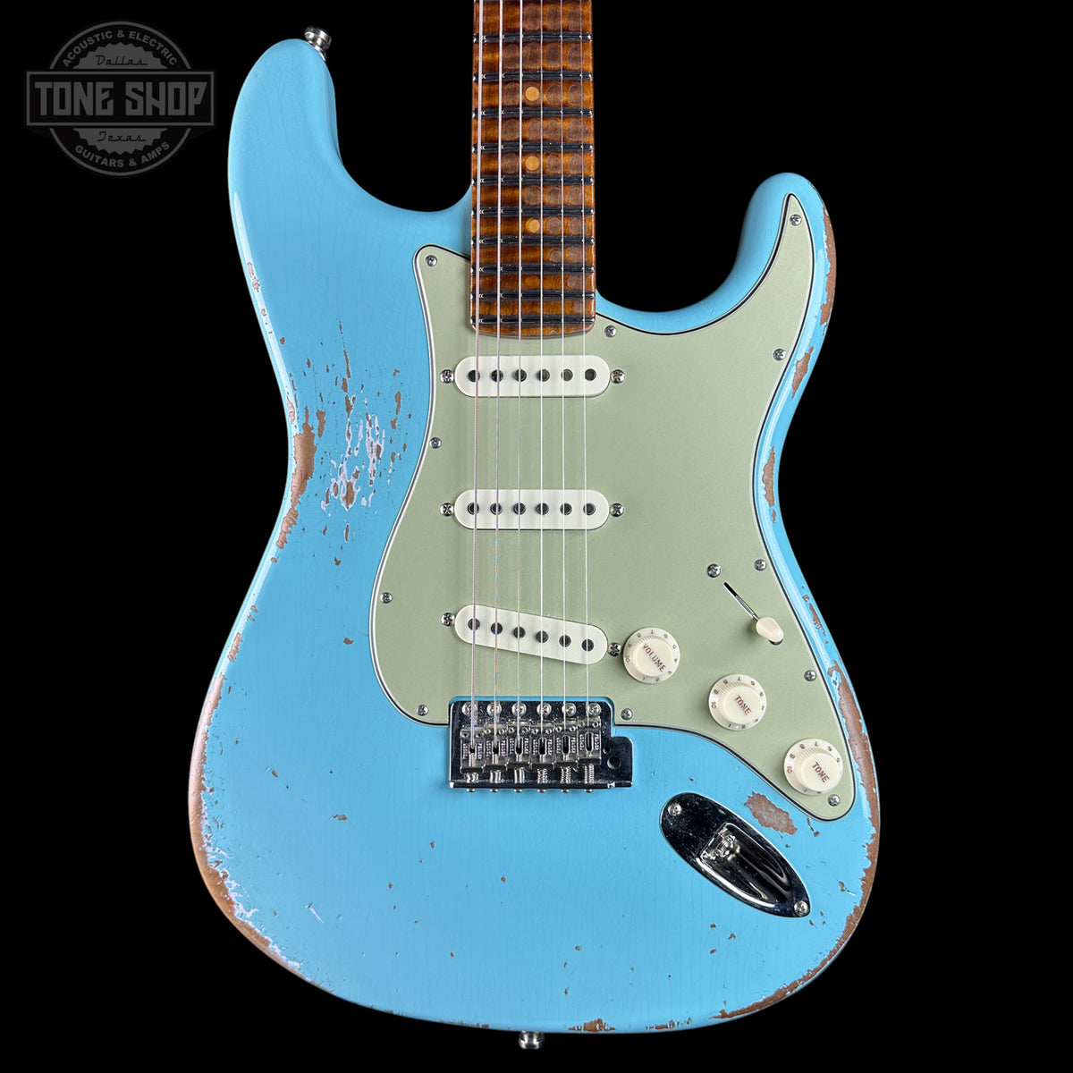 A light blue electric guitar with a distressed finish, featuring a pale green pickguard, white control knobs, and a brown fretboard, shown against a black background with a Tone Shop watermark.